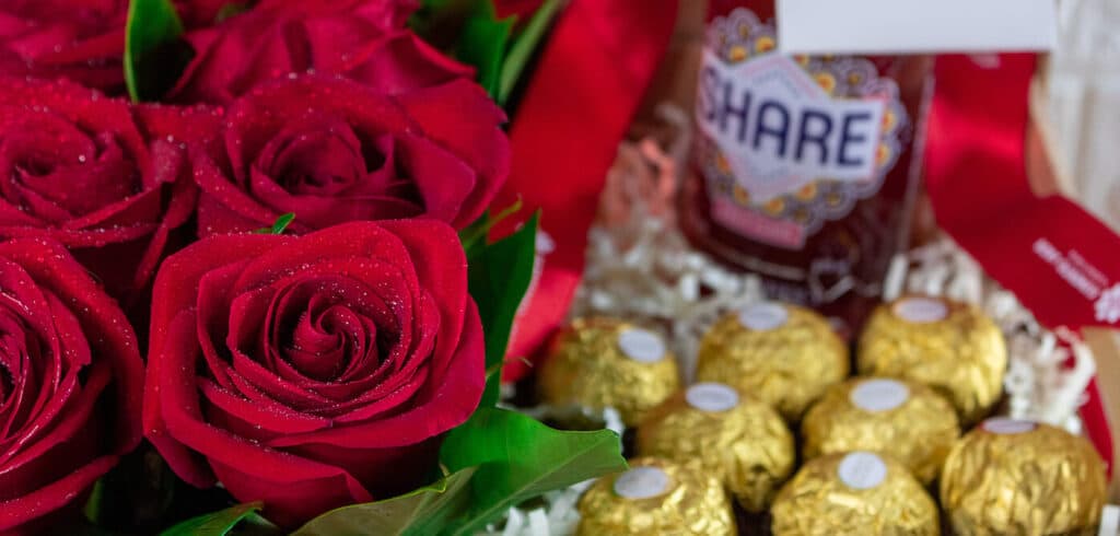 Primerísimo primer plano de regalo donde contiene varias rosas, chocolates y una bebida.