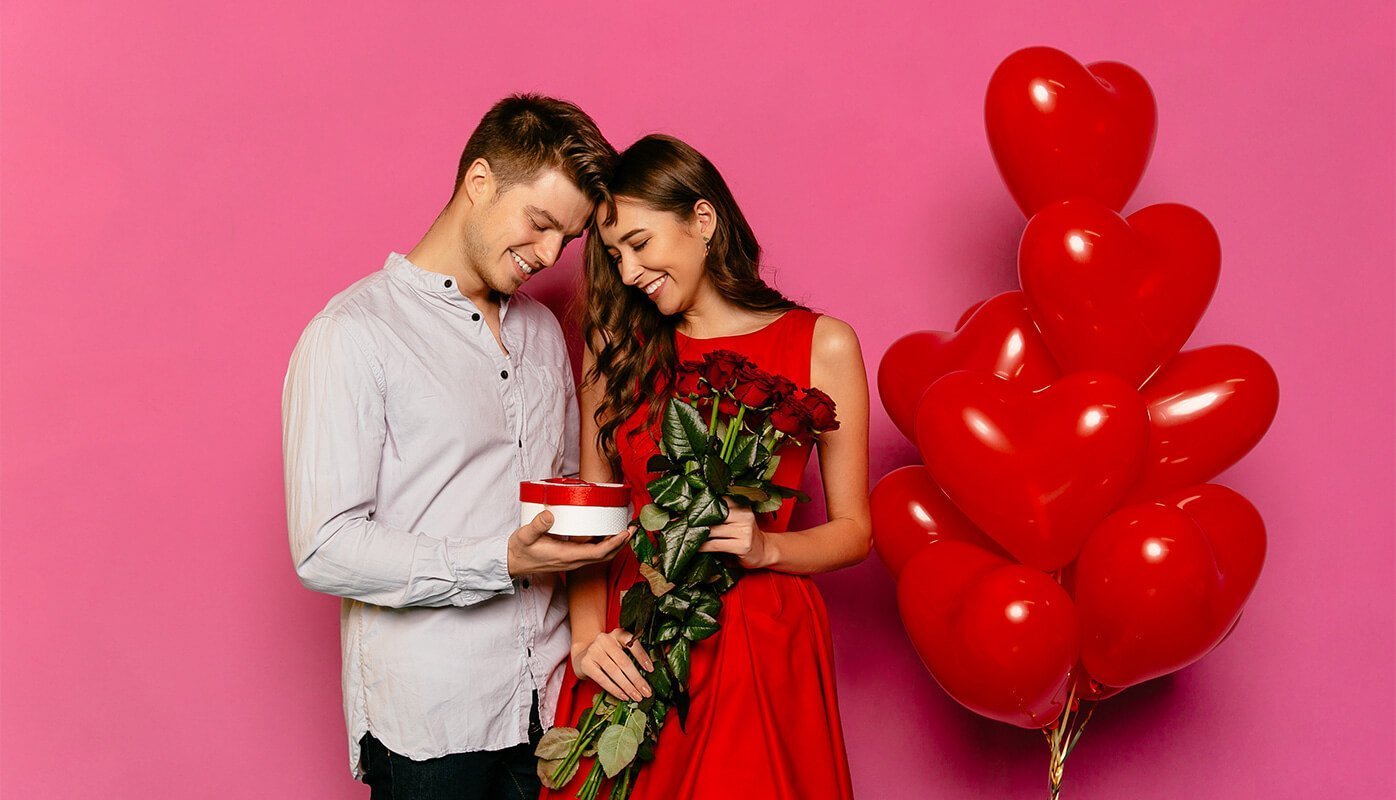 Pareja donde el chico está regalando flores, chocolates y globos a su enamorada